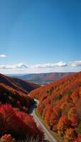 Wide shot of picturesque countryside scene featuring colorful autumn landscape and winding path to quaint village beneath clear sky photo