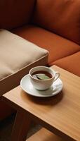 A teacup featuring a leaf rests on a nearby table beside a couch photo