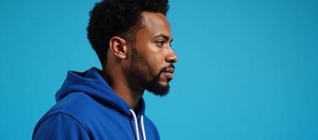 An African American man sporting an afrostyle hairdo and dressed in a hoodie stands against an isolated blue backdrop photo