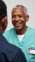 An elderly AfricanAmerican man in his 70s wears a nurses uniform and smiles joyfully sporting short white hair photo