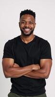 A smiling African American man poses on a white backdrop with crossed arms photo