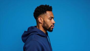 An African American man sporting an afrostyle hairdo and dressed in a hoodie stands against an isolated blue backdrop photo