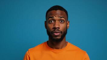 Expressive portrait of confused African American man in orange against blue backdrop photo
