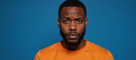 Expressive portrait of confused African American man in orange against blue backdrop photo