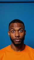 Expressive portrait of confused African American man in orange against blue backdrop photo