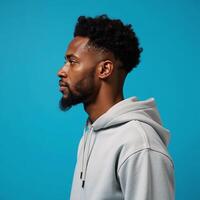 An African American man sporting an afrostyle hairdo and dressed in a hoodie stands against an isolated blue backdrop photo