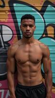 Young man in muscular form poses against graffitied backdrop AfricanAmerican photo