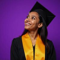 A smiling thoughtful young AfricanAmerican woman is depicted in a graduation cap and gown standing before a vibrant purple backdrop photo