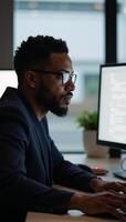 An African American male IT professional is portrayed while intensely focusing on coding tasks within his cybersecuritycentered workspace reflected in his glasses photo