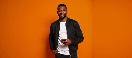 An attractive African American man holding a phone on an orange backdrop depicting Halloween or Thanksgiving themes photo