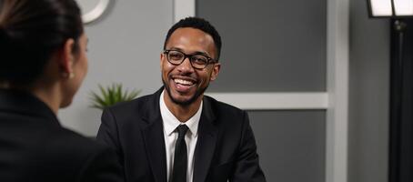 Medium shot Blacksuited man in glasses conversing with woman at a pod recording table in a studio photo
