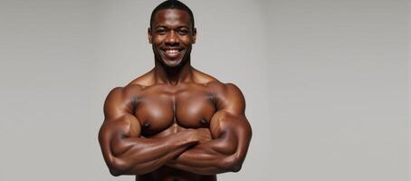 An athletic Black man stands with crossed arms and a smile against a backdrop photo