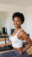 A joyful Black woman smiles as she practices Pilates at home amidst a wellequipped fitness studio photo