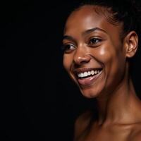 Closeup portrait of a youthful radiant African American woman with smooth skin and a bright smile gazing off into the distance on a dark backdrop photo