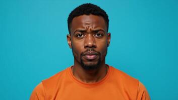 Portrait of puzzled African American man in orange top set against vibrant blue backdrop photo