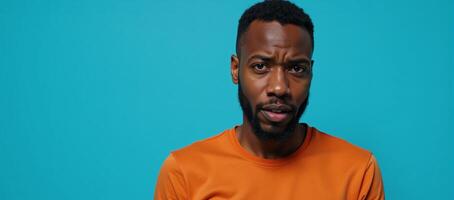 Portrait of puzzled African American man in orange top set against vibrant blue backdrop photo