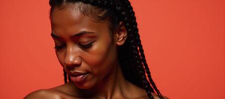 Closeup portrait of a radiant Black woman with long braids in a vibrant coral backdrop eyes closed gazing downwards photo