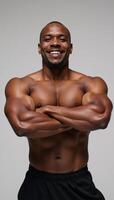 An athletic Black man stands with crossed arms and a smile against a backdrop photo