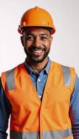 A confident AfricanAmerican man dons safety gear smiling brightly while clad in an eyecatching orange vest and helmet set against a stark monochrome white backdrop photo