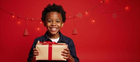 Portrait of joyful AfricanAmerican boy with wrapped present against festive red backdrop celebrating Christmas or a birthday theme including copy space for text overlay photo