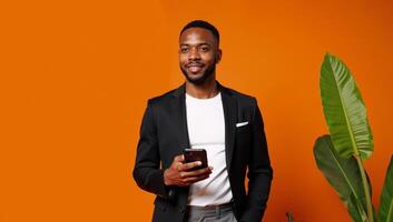 An attractive African American man holding a phone on an orange backdrop depicting Halloween or Thanksgiving themes photo