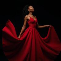 A striking African American woman wears an eyecatching flowing red gown against a black backdrop photo