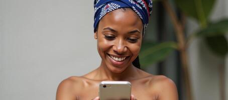 an AfricanAmerican woman wearing a head wrap using her phone with a smile photo