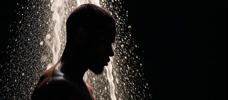 A cooling shower scene featuring a black AfricanAmerican man in silhouette with refreshing water pouring over him photo
