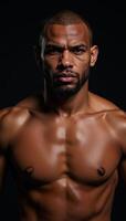 A muscular African American MMA fighter looks intensely into the camera with his head covered sweating against a dark backdrop photo