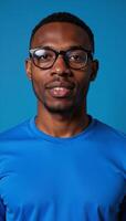 Isolated portrait of an African American man wearing a blue tshirt and glasses against a blue backdrop photo