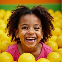 A joyful African American girl is captured laughing while playfully submerged in a vibrant yellow ball pit photo