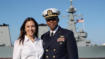 A veteran AfricanAmerican Navy Officer stands proudly with spouse by warship beneath the American flag on Veterans Day photo