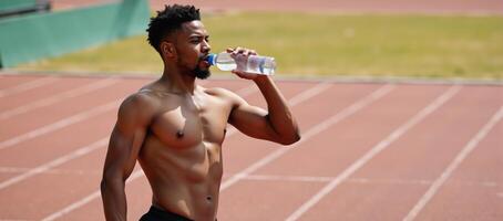 Young African American athlete sips water from a plastic bottle during practice on a running track photo