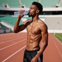 Young African American athlete sips water from a plastic bottle during practice on a running track photo