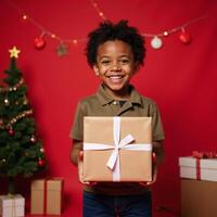 Portrait of joyful AfricanAmerican boy with wrapped present against festive red backdrop celebrating Christmas or a birthday theme including copy space for text overlay photo