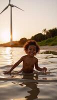 An African American child enjoys playing in water during sunset beside wind turbines showcasing an ecofriendly energy theme blending human connection with technology photo