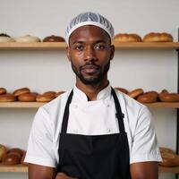 A young black baker dons hairnet apron amidst shelves of fresh pastries gazing seriously into camera photo