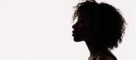 A contemplative black silhouette of an African American woman with curly hair illuminated by backlighting and gaze to the side on a white background photo