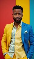 An AfricanAmerican man stands out in vibrant colors wearing a yellow and blue ensemble against a backdrop of dynamic hues photo