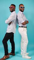 Cheerful African American duo pose confidently backtoback against a bright blue backdrop showcasing stylish summer outfits with eyecatching sunglasses photo