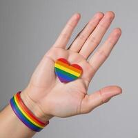 A hand wearing an LGBTQ Pride rainbowwristed band is shown against a backdrop of a heart shaped rainbow flag symbolizing Gay Pride photo
