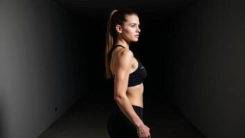Woman in sports bra ponytail stands sternly within a tunnel photo