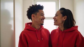 A young smiling African American couple shares laughter inside a bathroom while wearing matching red hoodies photo