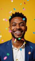 Joyful African American Man amidst colorful confetti shower against a bright yellow backdrop photo