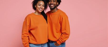 Two African American individuals dressed casually in bright orange sweatshirts and jeans pose against a muted pastel background photo