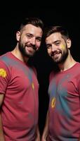 Black White portrait showcases a vibrant colorfully dressed gay couple posing playfully with paint on their faces against a stark black backdrop photo