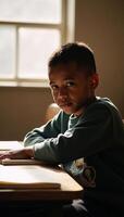 An AfricanAmerican boy with a distraught look sits in daylight casting a warm glow on his troubled expression within a school setting photo