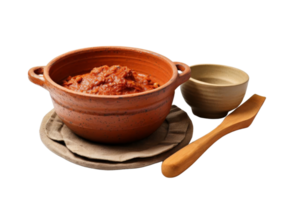A bowl of red sauce sits on a plate with a spoon next to it. The bowl is made of clay and the spoon is wooden. Concept of comfort and warmth, as the red sauce png