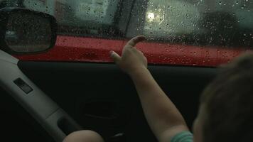 A little boy drawing patterns on the window. A child in the car playing with drops after the rain. video