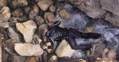 Corpse of man on shore. Stock. Body of man on rocks with waves on shore. Bandit is lying unconscious on shore video